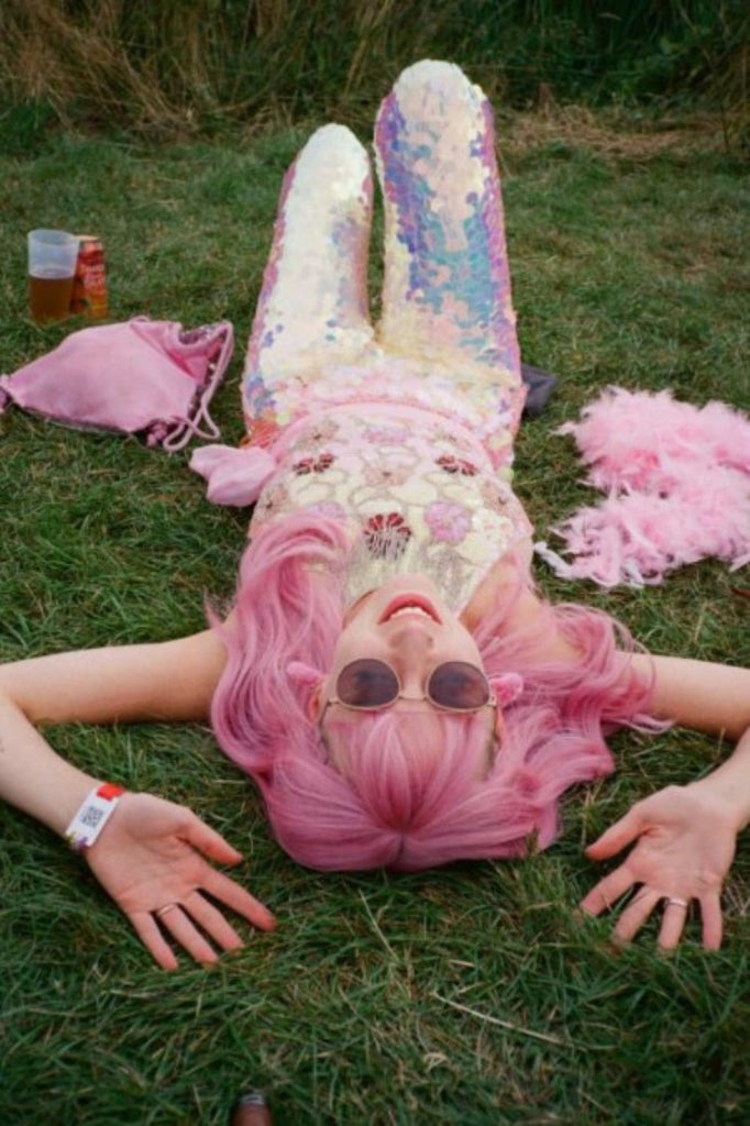 Pink haired girl lying down in green grass at a festival wearing sunglasses, many pink items of clothing and Rosa Bloom White Opal Sequin Indus Leggings