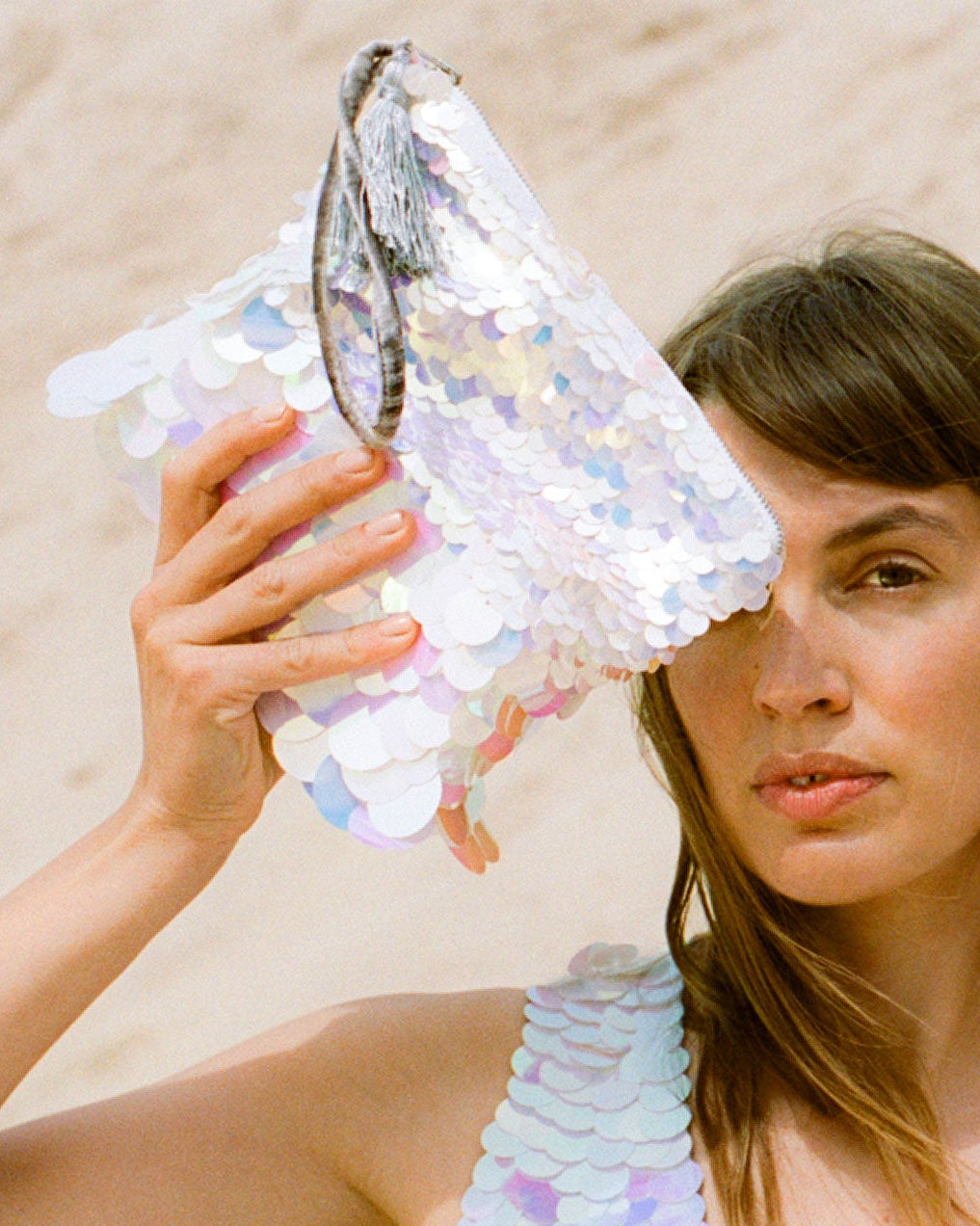Woman holding a sequined purse against a sandy background