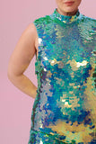 A crop of the top half of a woman, wearing an all-in-one sequin stretchy festival jumpsuit made with large round holographic Rosa Bloom sequins. The Iris jumpsuit sequins glisten all over, creating a mix of shimmering colours of soft mint green and sage.