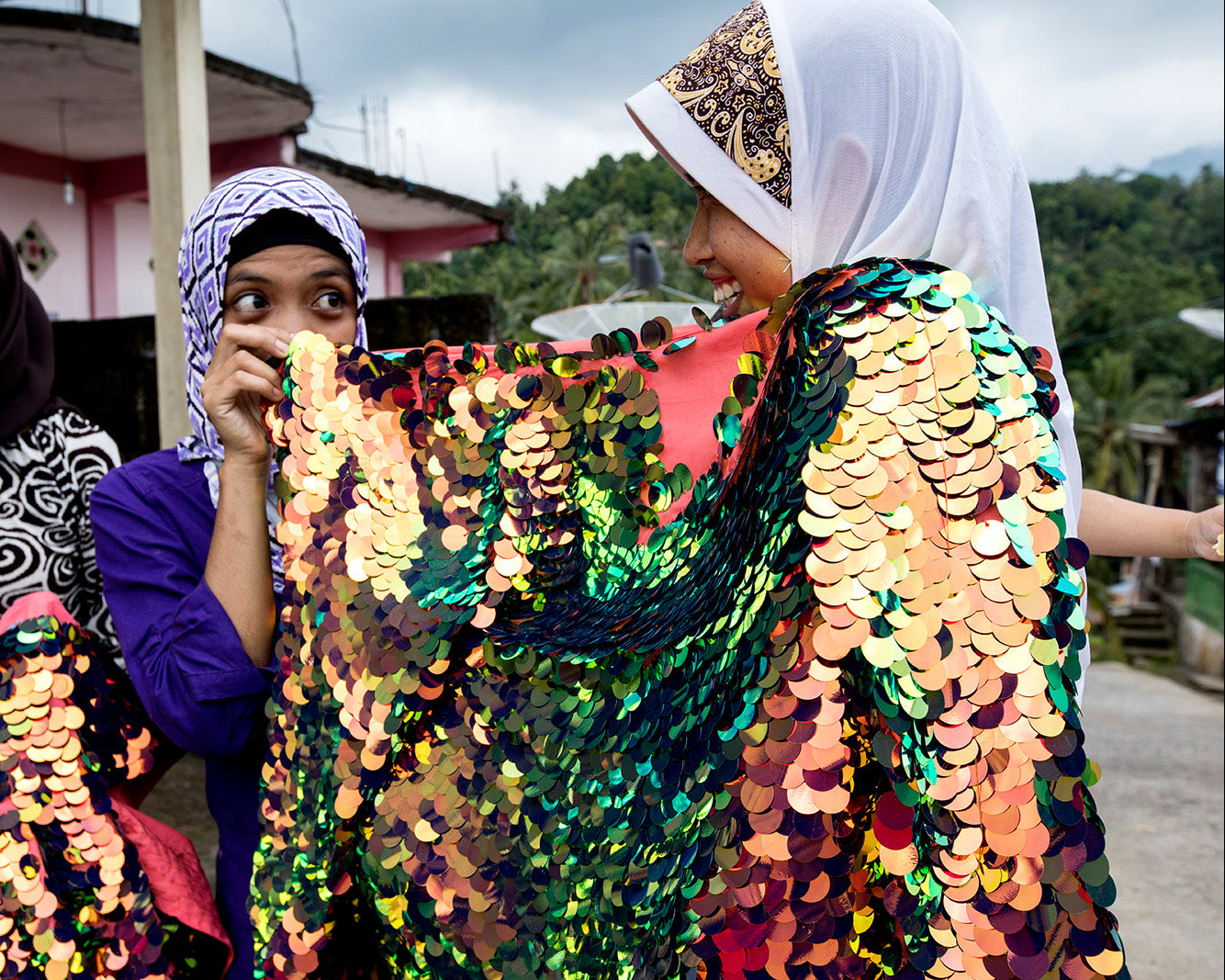 Two women holding a sequin embroidered garment and laughing in an outdoor setting