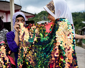 Two women holding a sequin embroidered garment and laughing in an outdoor setting
