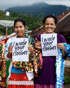 Three people holding hand-stitched sequin garments and signs reading 'I made your clothes' standing in a scenic outdoor setting