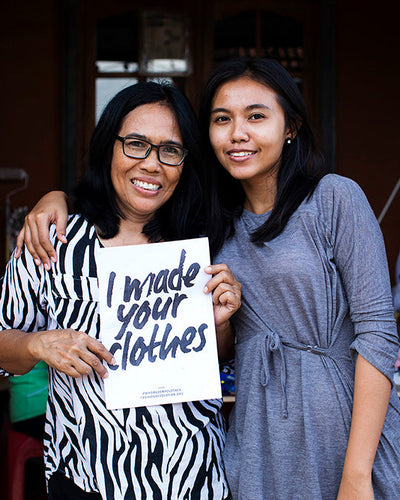 Two women holding a sign that reads 'I made your clothes'.