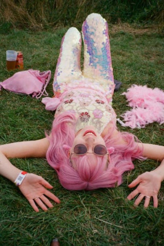 Pink haired girl lying down in green grass at a festival wearing sunglasses, many pink items of clothing and Rosa Bloom White Opal Sequin Indus Leggings