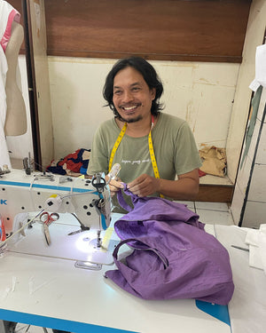 Man working on a sewing machine with a purple garment in a workshop.