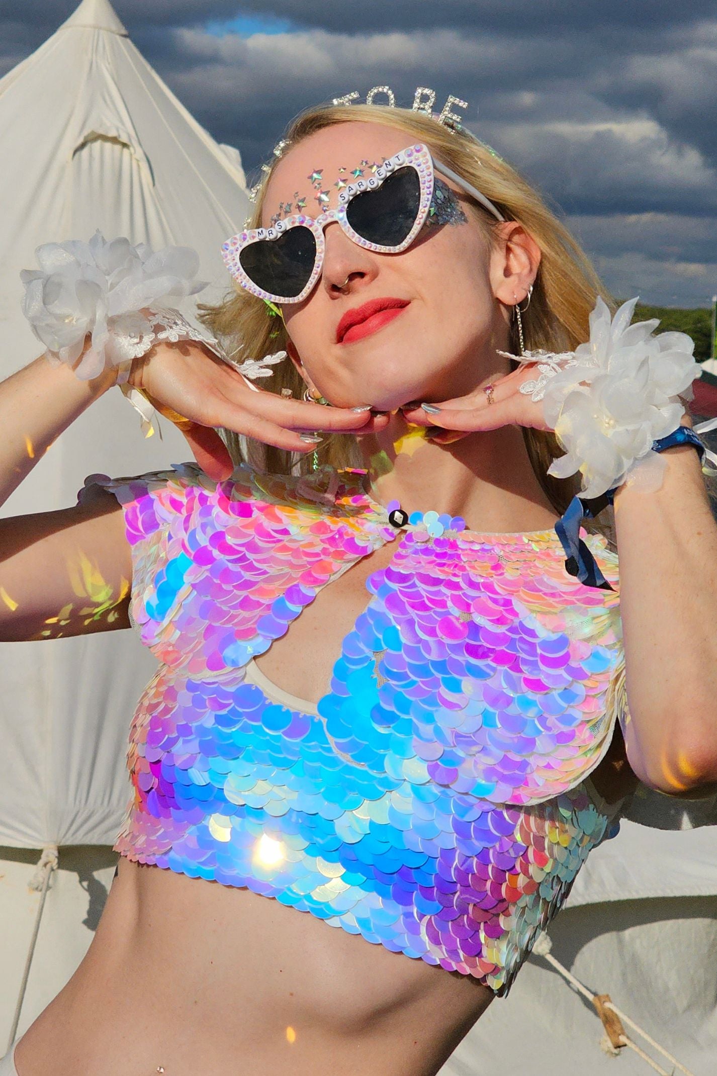 Smiling blonde woman on her hen do at a festival posing with her hands framing her face wearing a Rosa Bloom Inti Opal Sequin Cape and Twinks Opal sequin crop top