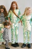 A group of four children who look like they are having fun in an outdoor park setting. Three children are wearing a mix of chameleon mint green large round sequin festival kids t-shirts and leggings. The small child is wearing a black and white geometric pair of childrens festival leggings with a matching short sleeve black and white geometric tri-print t-shirt by Rosa Bloom. 