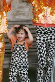  A cropped image of a small child with short dark hair who has her hands above her head. She is wearing black and white tri-print dungarees in the Rosa Bloom tri-print design with a peach coloured childrens t-shirt. Cropped from the photo, there are two older children wearing matching tri print leggings, along with the irridescent dreamy fox sequin outfits for kids of matching leggings and t-shirts. 