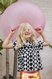  An image of a child in a brightly lit outdoor festival circus space, playing with large pink balloon. He is wearing Rosa Blooom Sonny T-shirt in Tri-print design with fox sequin children leggings. 