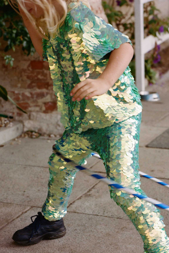 A cropped image of a small child who is playing with a stripy hula hoop.  He is wearing childrens sequin festival  leggings and a matching chameleon mint green sequin t-shirt. 