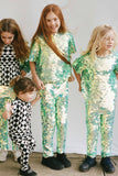 Four children in a brightly lit outdoor space  having fun with festival, party vibes. They are all wearing Rosa Bloom chameleon mint green, shimmering sequin clothing and bold graphic tri-print geometric design. They are wearing the chameleon sequin leggings and matching sequin children’s t-shirts. The little one is dressed in Childrenswear Rosa Bloom tri-print in black and white.