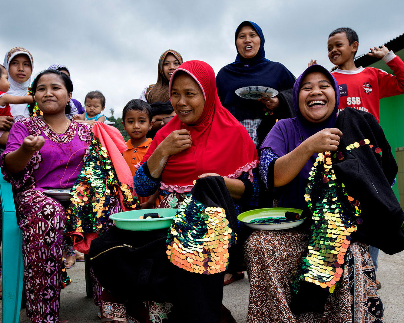 Group of people outdoors with colourful sequin clothing that they are stitching.