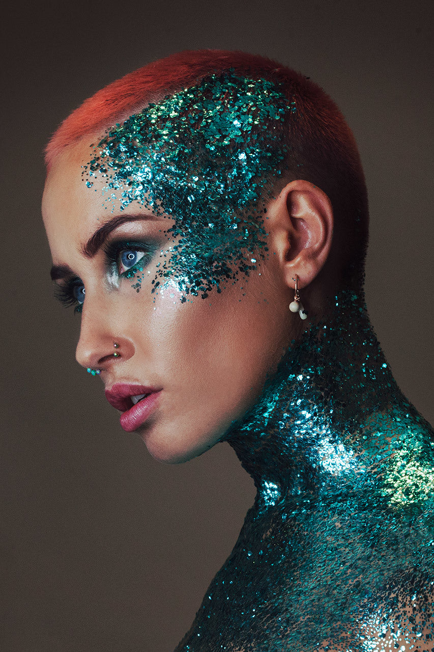 A woman's face, neck and shoulders are adorned with aqua trip cosmetic biodegradable glitter