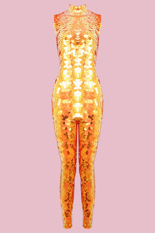 An all-in-one sequin stretchy festival jumpsuit made with large round holographic Rosa Bloom sequins. The Fox jumpsuit in front of a pink background, glistens all over in this colour way, creating a mix of shimmering sequin colours of gold and yellow that sparkles in the light.