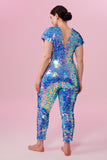 Dark haired model with hair tied back wearing a Rosa Bloom sequin Aphrodite jumpsuit in Amethyst