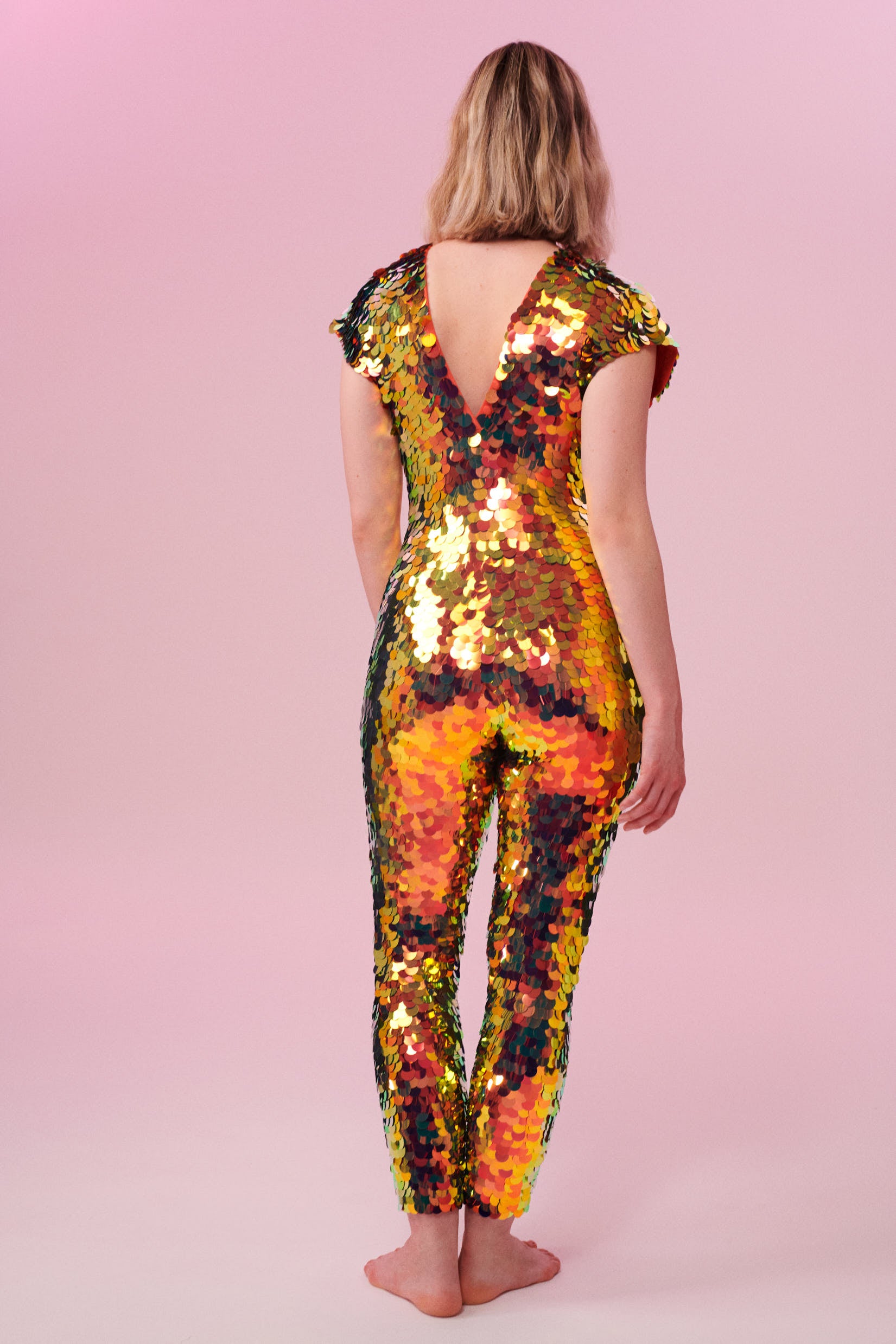 Blonde haired model wearing a Rosa Bloom Aphrodite sequin jumpsuit in Ember