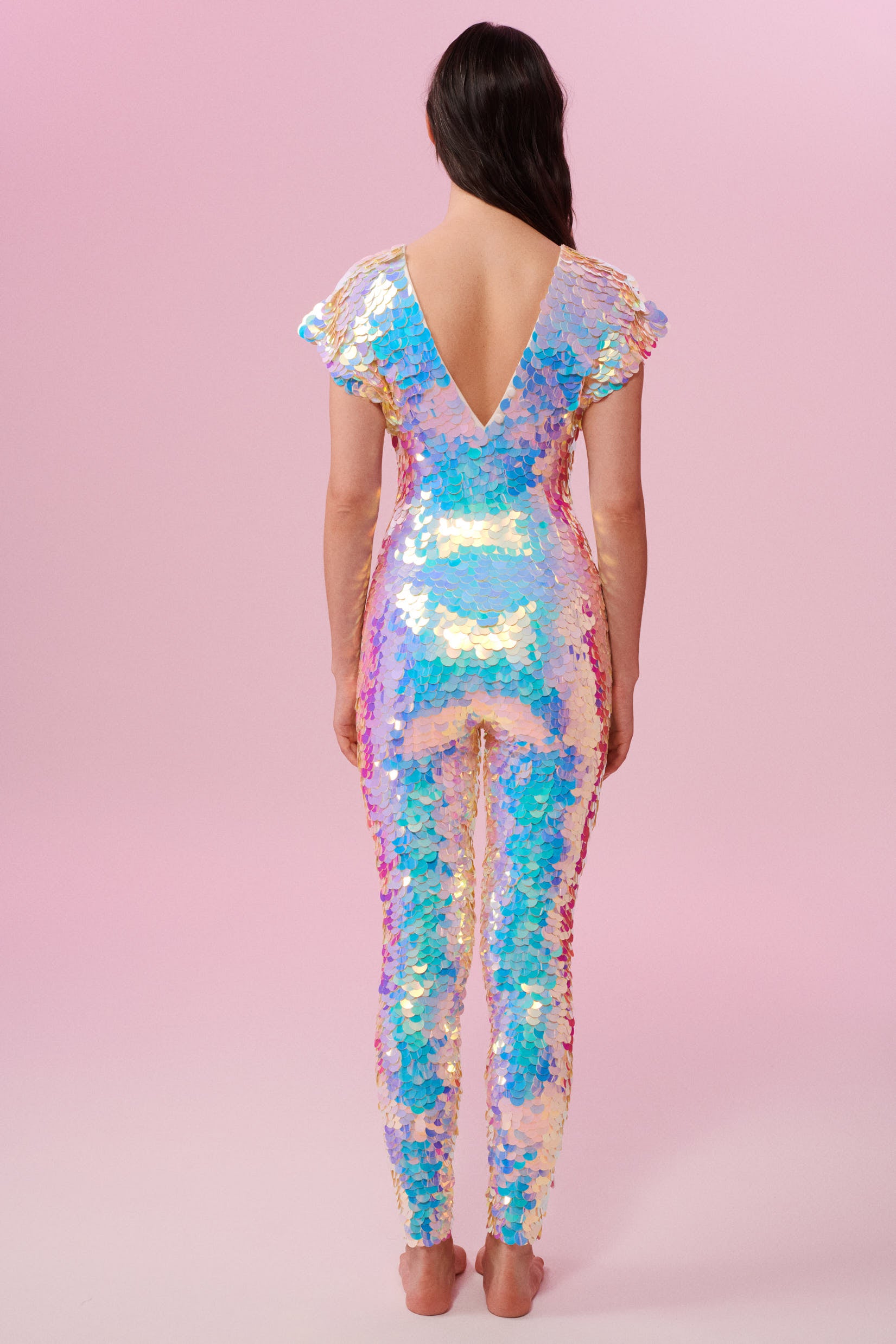 Back view of a woman wearing the Rosa Bloom Aphrodite jumpsuit embellished in hand sewn sparkly opal white sequins with a pink-blue shine.