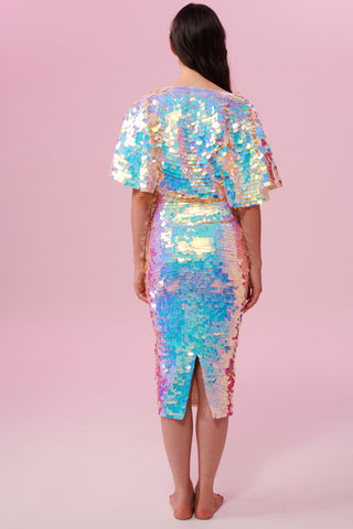 A woman standing with her back to you wearing an opal sequin top with large cape sleeves covered in large round holographic purple,pink, blue and white coloured Rosa Bloom sequins. She is also wearing a skirt made from the same large coloured sequins.