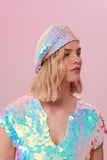 A side on view of a woman with short blonde hair, wearing a Grace sequin beret made from small round holographic sequins with hues of lilac purple, light blue and soft pinks. The festival sequin hat matches the sequin top that the model is wearing. The Opal sequins by Rosa Bloom glisten, creating a mix of shimmering colours.  