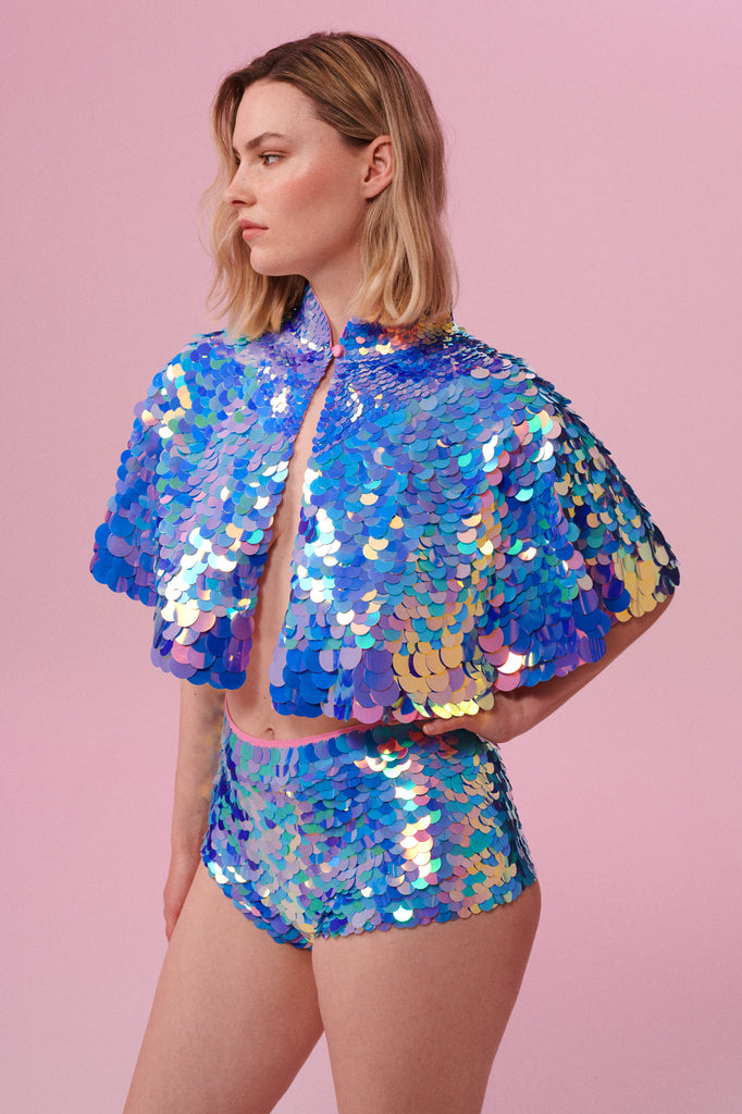 Side view of a woman wearing Rosa Bloom Shimmering Sequin Cape with pink blue and purple sequins