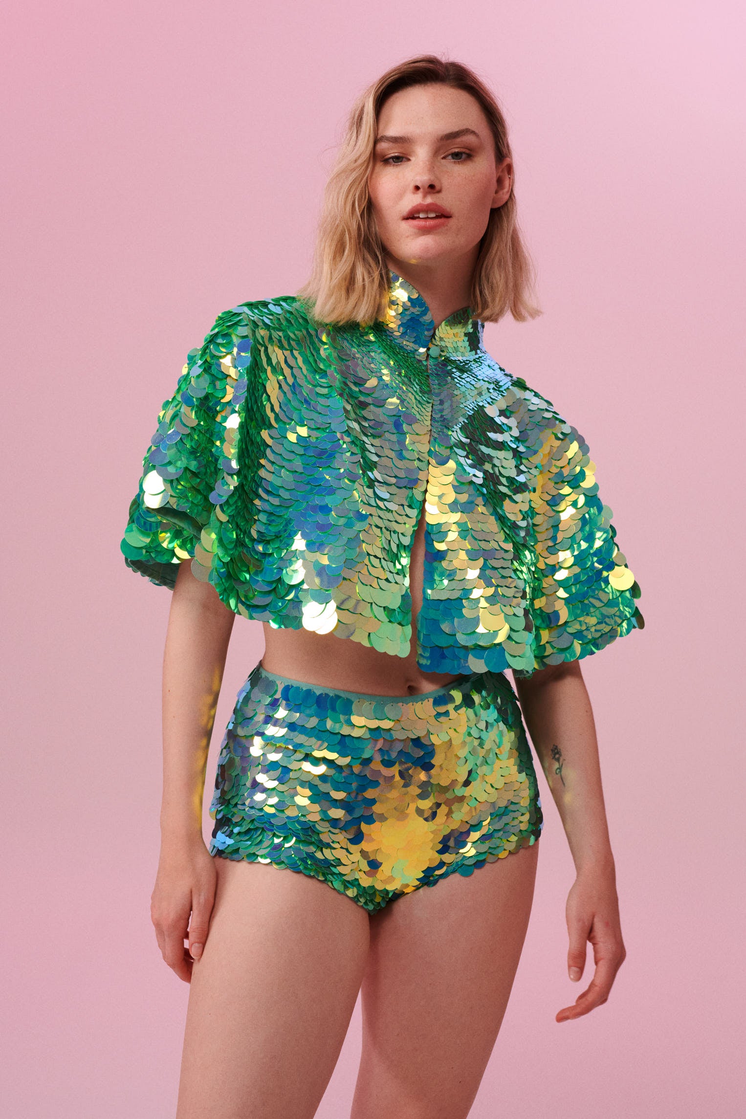Front view of a woman wearing Rosa Bloom Shimmering Sequin Cape with light green sequins