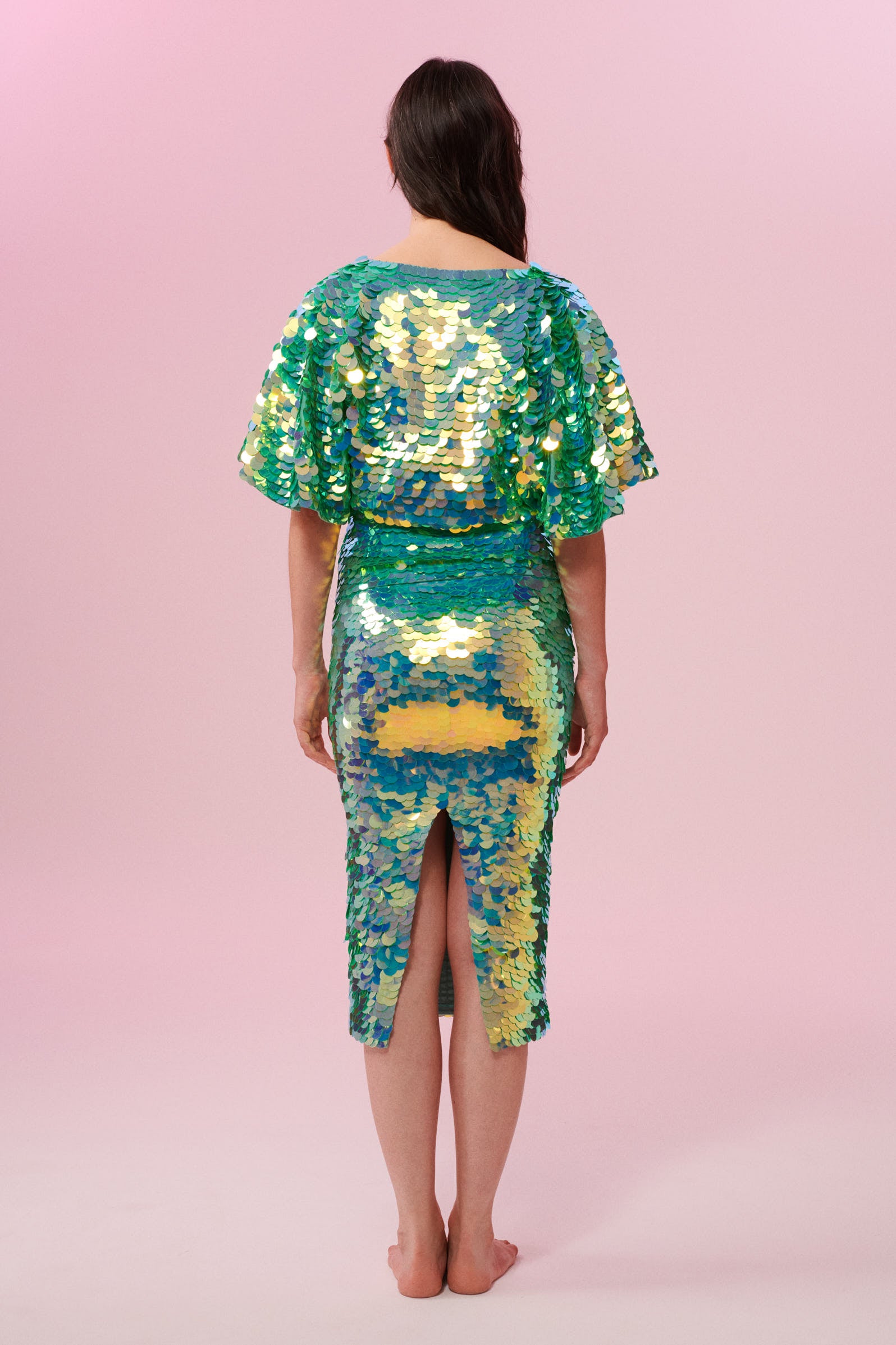 Back view of a dark haired woman wearing a Rosa Bloom green sequin mid length sequin tube skirt