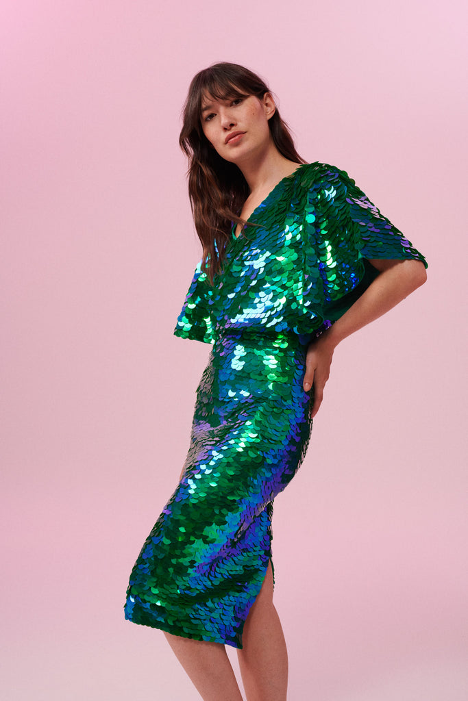 Side view of a dark haired woman wearing a Rosa Bloom emerald green sequin mid length sequin tube skirt