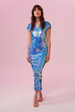 A woman facing towards you wearing a blue and pink  long, figure hugging sequin dress with small capped sleeves covered completely in large round holographic soft rose pink, lilac, and cornflower blue coloured Rosa Bloom sequins.