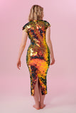A woman standing with her back to the viewer wearing an iridescent golden sequin long dress. A figure hugging  dress down to the ankles with small capped sleeves completely covered in large round holographic Rosa Bloom sequins. The sequins glisten, creating a mix of shimmering colours of burnt orange, yellow, gold and warm red making this sequin dress glow when worn. 