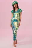 A woman with long hair, facing the viewer wearing an iridescent pale green sequin long dress. A figure hugging  dress down to the ankles with small capped sleeves completely covered in large round holographic Rosa Bloom sequins. The sequin colours shine in the studio lights, creating a mix of shimmering colours of sage green, mint and a warm peachy gold making this sequin dress glow when worn. The model is also wearing a matching sequinned beret hat.