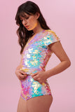 A side on view of a woman with brown hair, wearing a sequin stretchy top with capped sleeves made with large round holographic Rosa Bloom sequins. The Gwen sequins glisten, creating a mix of shimmering colours of soft gold, aqua, lilac, and peach. The model is also wearing matching high waisted, stretchy festival sequin shorts in the same matching sequin colour way.