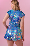 A rear view of a woman with short blonde hair, wearing high waisted festival sequin shorts and a matching sequin top made with large round holographic Rosa Bloom sequins. The Amethyst  sequins glisten in the light, creating a mix of shimmering colours of lilac purple, light blue and soft pinks. 