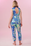 A rear view of a woman with short blonde hair, wearing an all-in-one sequin stretchy festival jumpsuit made with large round holographic Rosa Bloom sequins. The Iris sequins glisten, creating a mix of shimmering colours of pink, blue and purple.  