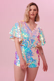A model with short blonde hair wearing a Rosa Bloom sequin Mella romper playsuit in the Opal design. A mix of white, pinks and blue sequins shimmer in the light showing the shorts and commanding cape sleeved festival outfit.  The all over iridescent disc sequins, as worn by Taylor Swift shimmers in the light.  