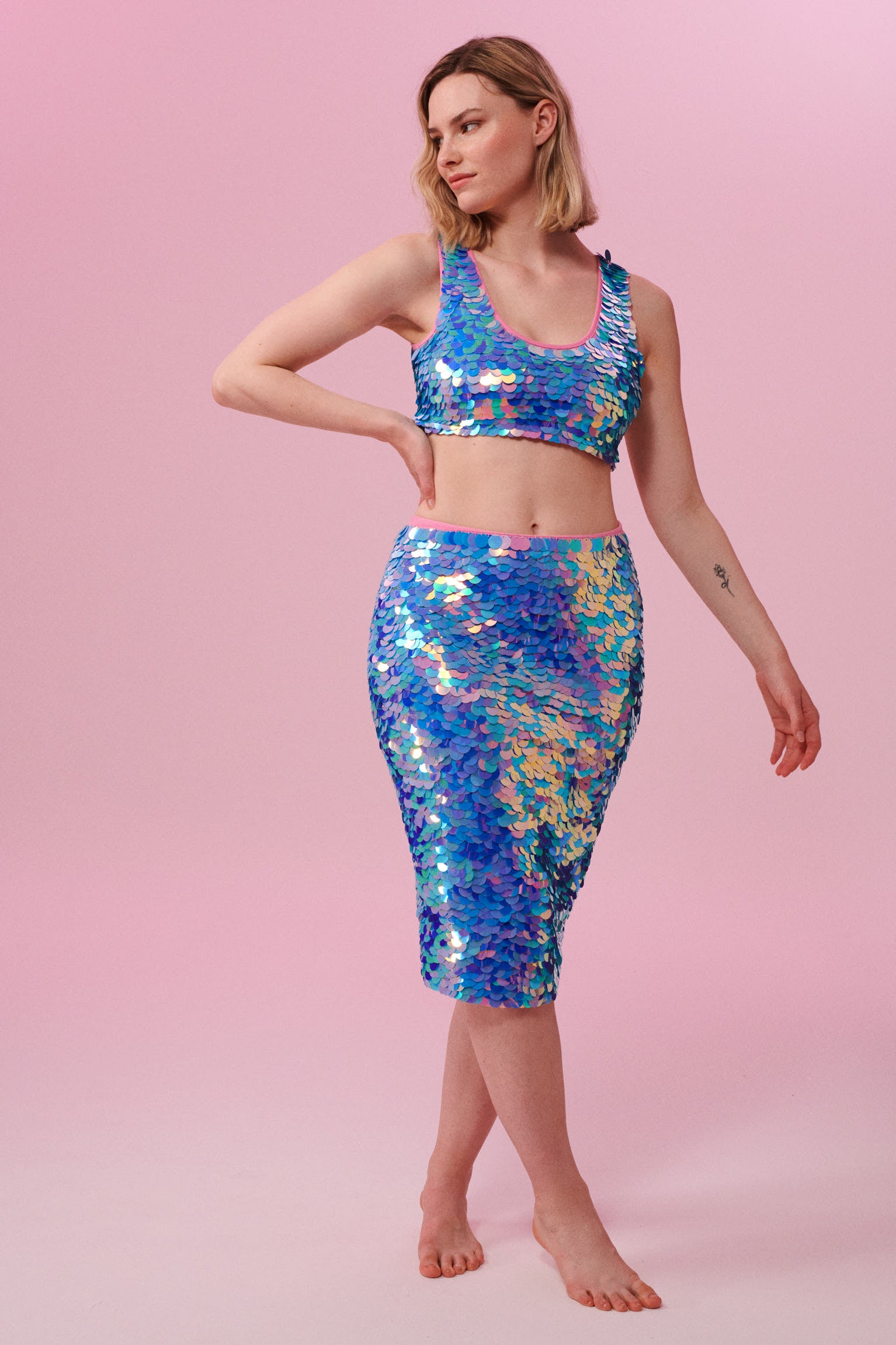 Front view of a blonde model wearing a Rosa Bloom blue and pink sequin mid length sequin tube skirt