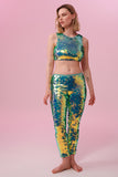 A woman wearing iridescent mint green stretchy sequin Indus leggings covered in large round holographic Rosa Bloom sequins. The sequins glisten, creating a mix of shimmering colours of pale green sequinned mint and warm peachy gold make this sequin glow. The model is also wearing a matching stretchy sequin vest top, in matching colours. This Chameleon sequin outfit looks like it is glowing. 