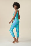Side view of a woman wearing the Rosa Bloom Electra jumpsuit in a mesmerising aqua blue. A stretchy jumpsuit with button fronted detail that hugs and contours her body embellishing her in sparkling sequins.