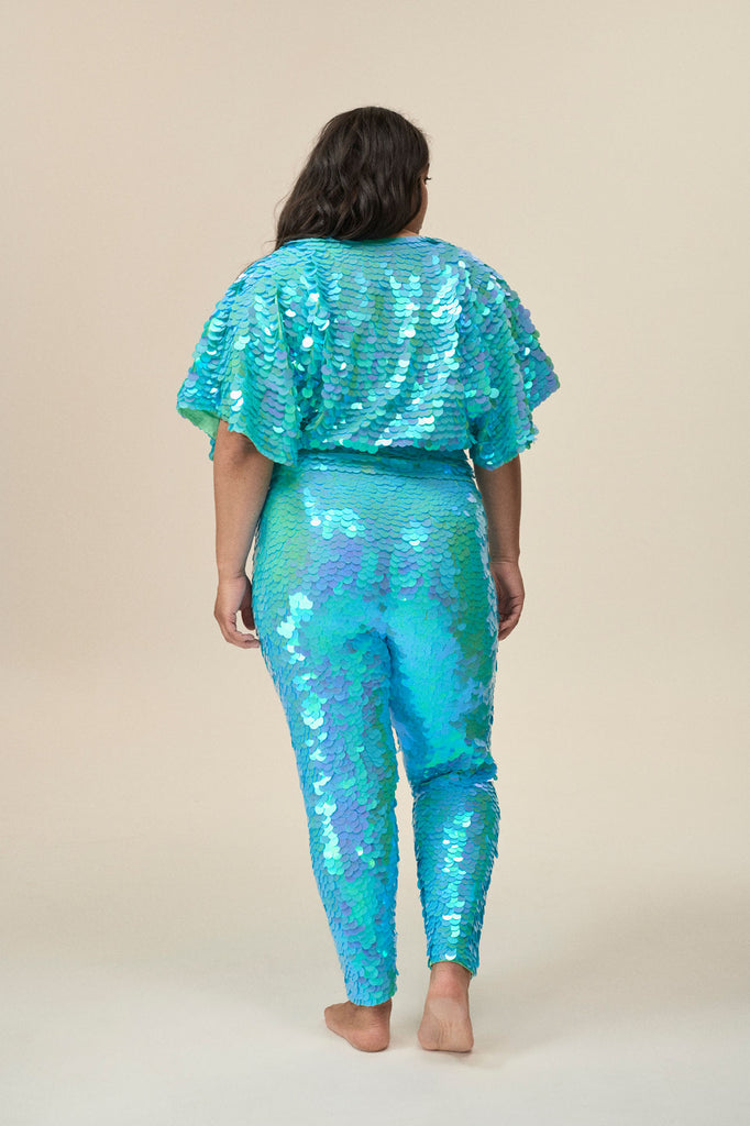 A rear view of a woman wearing a mint sequin top with large cape sleeves covered in large round holographic aqua blue coloured sequins.