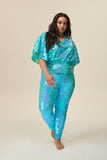 A woman facing and stepping towards you wearing a mint sequin top with large cape sleeves covered in large round holographic aqua blue coloured sequins.