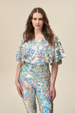 A woman wears a hologram silver sequin top with cape sleeves and matching silver sequin leggings. 