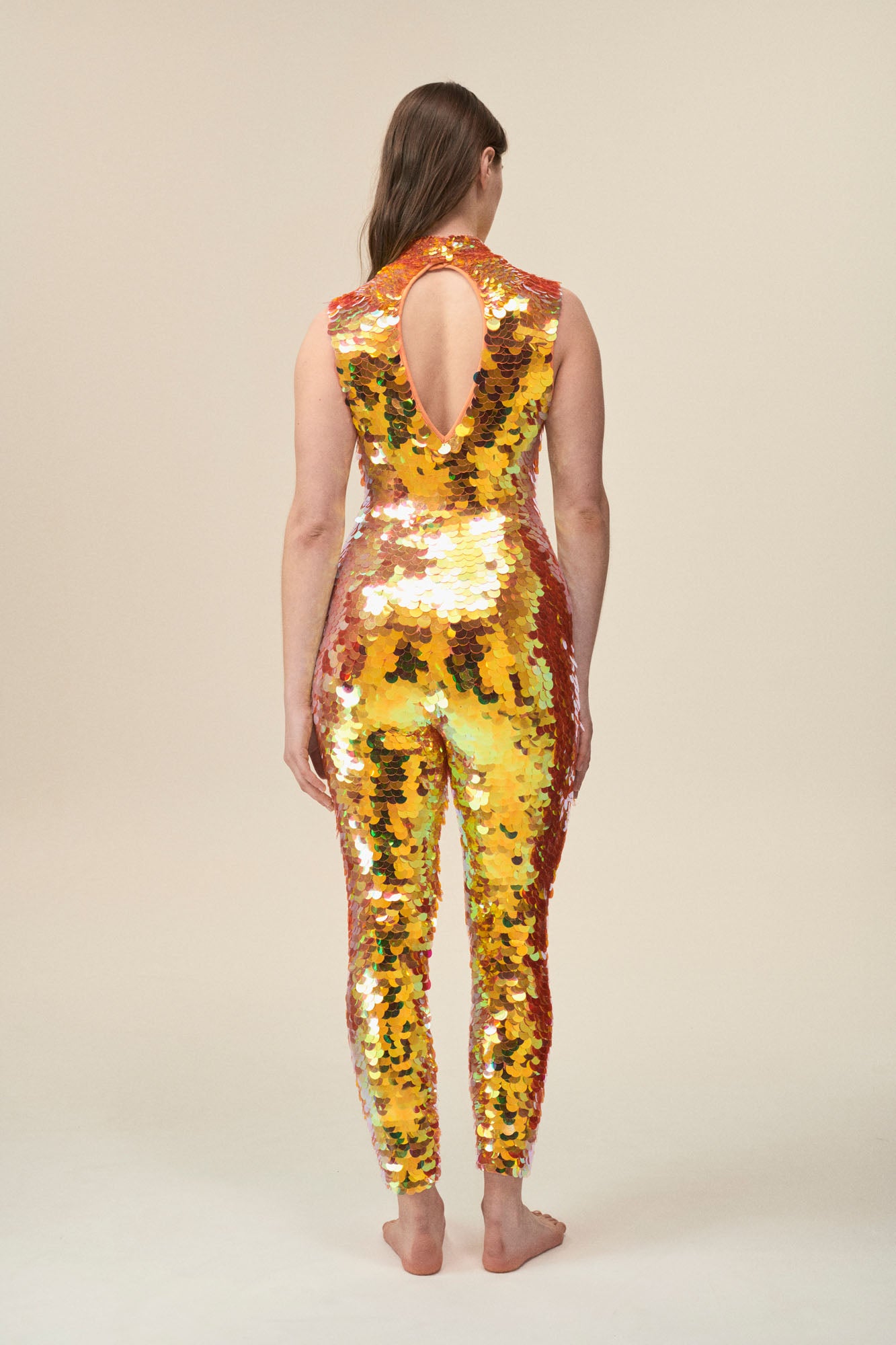 A back view of a woman wearing a high neck sequin jumpsuit covered in large round orange sequins.