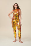 A woman stands with her hand on her hip and wears a dazzling orange sequin jumpsuit with a high neck. 