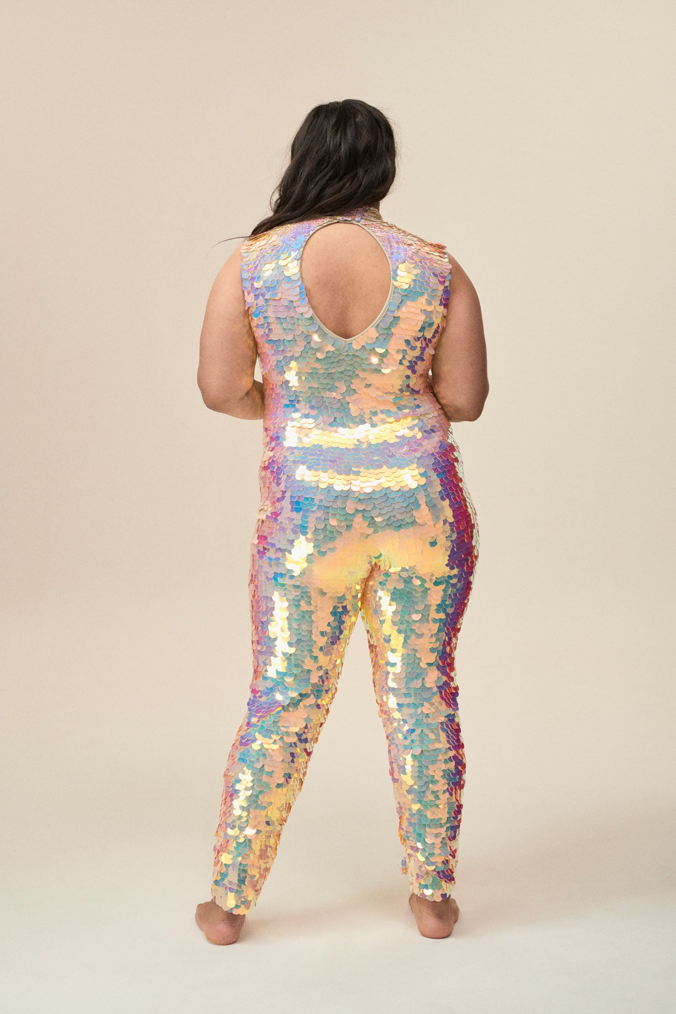 A back view of a woman wearing a plus-sized off-white sequin jumpsuit with a high neck collar and keyhole back detail. 