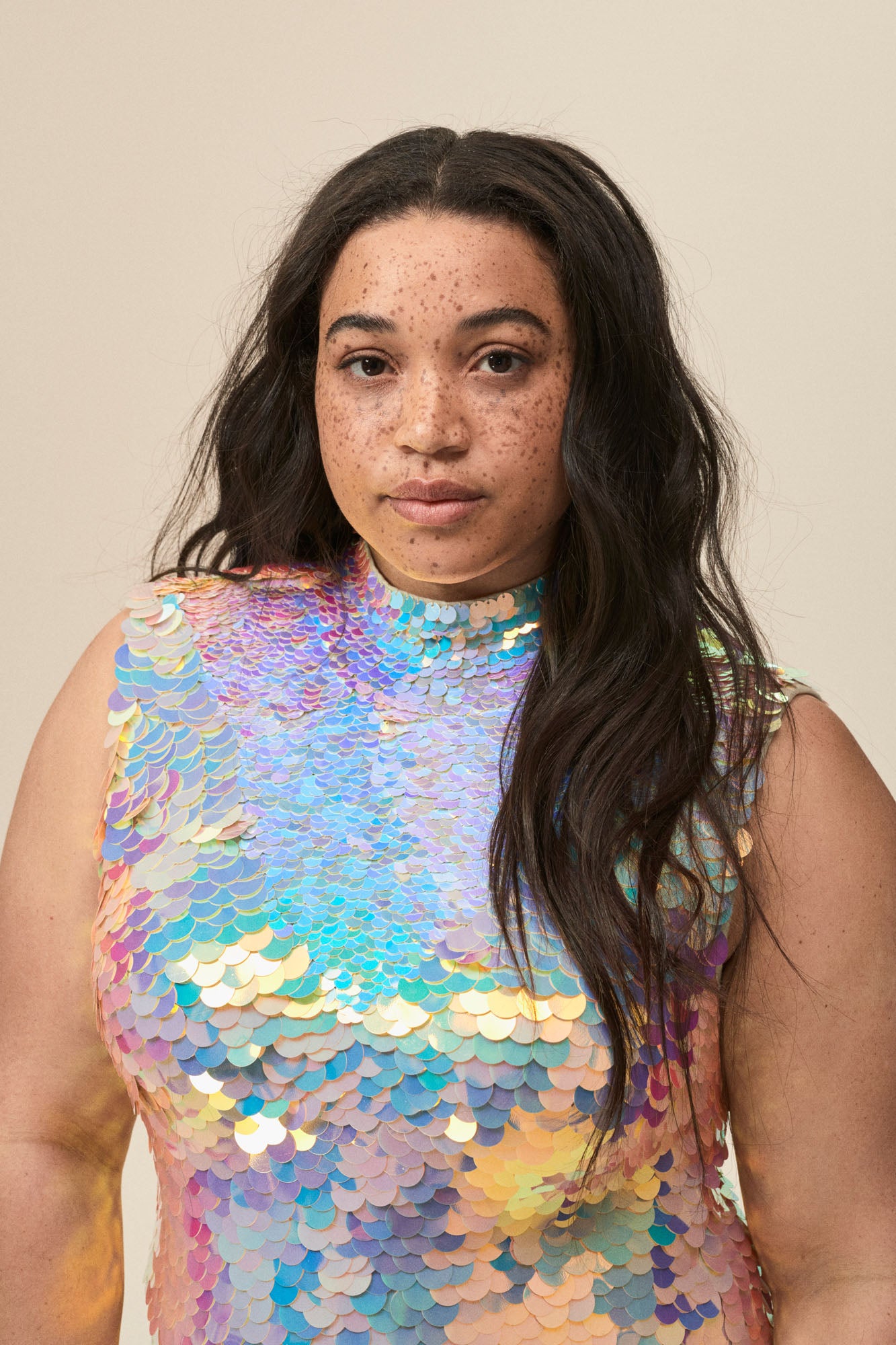  A portrait of a woman wearing a dazzling off-white sequin jumpsuit with a high neck collar.