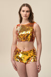 A woman faces you wearing stretchy Rosa Bloom Gigi hotpants with large sparkling orange sequins