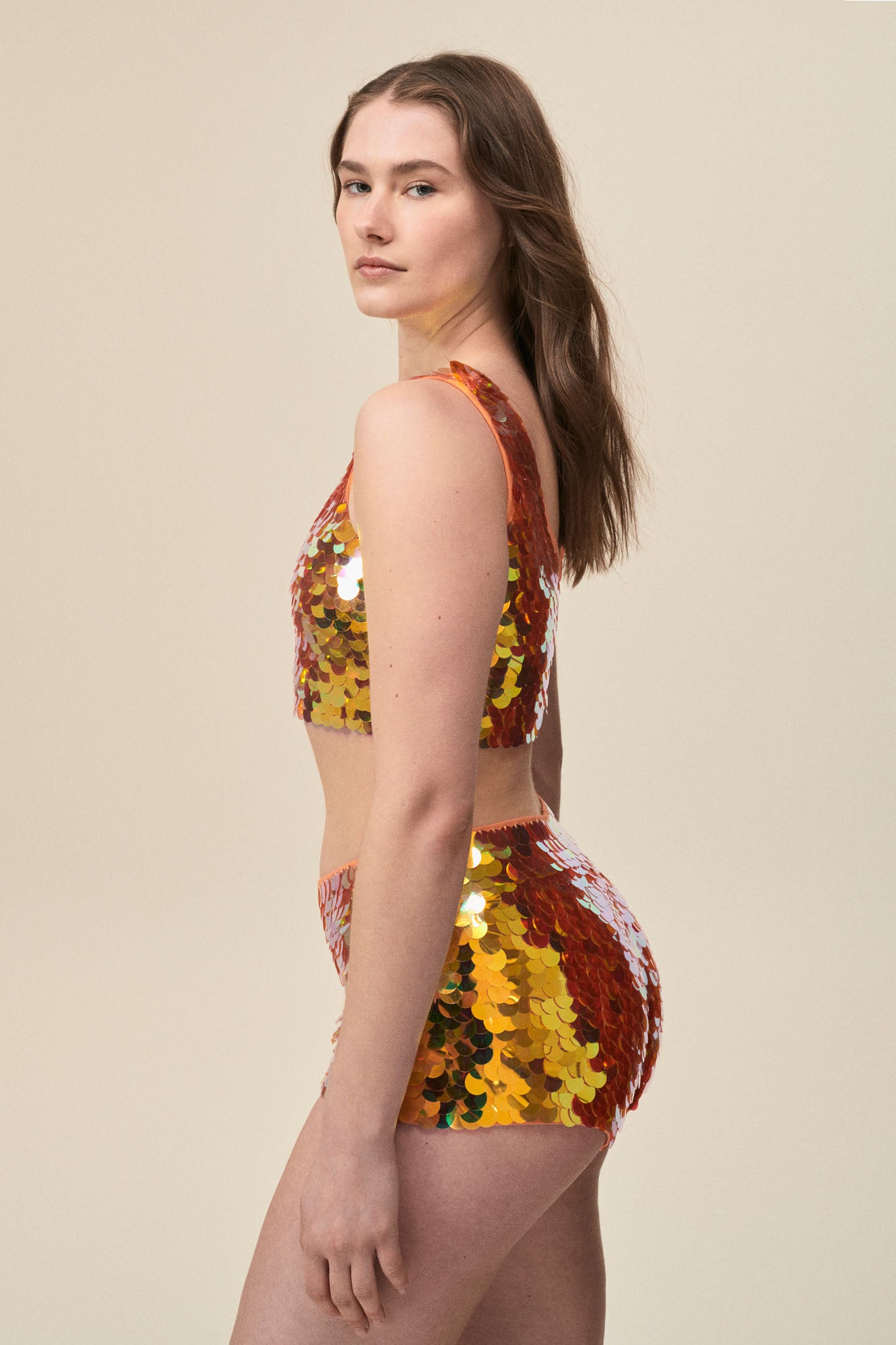 Side view of a woman wearing stretchy Rosa Bloom Gigi hotpants with large sparkling orange sequins