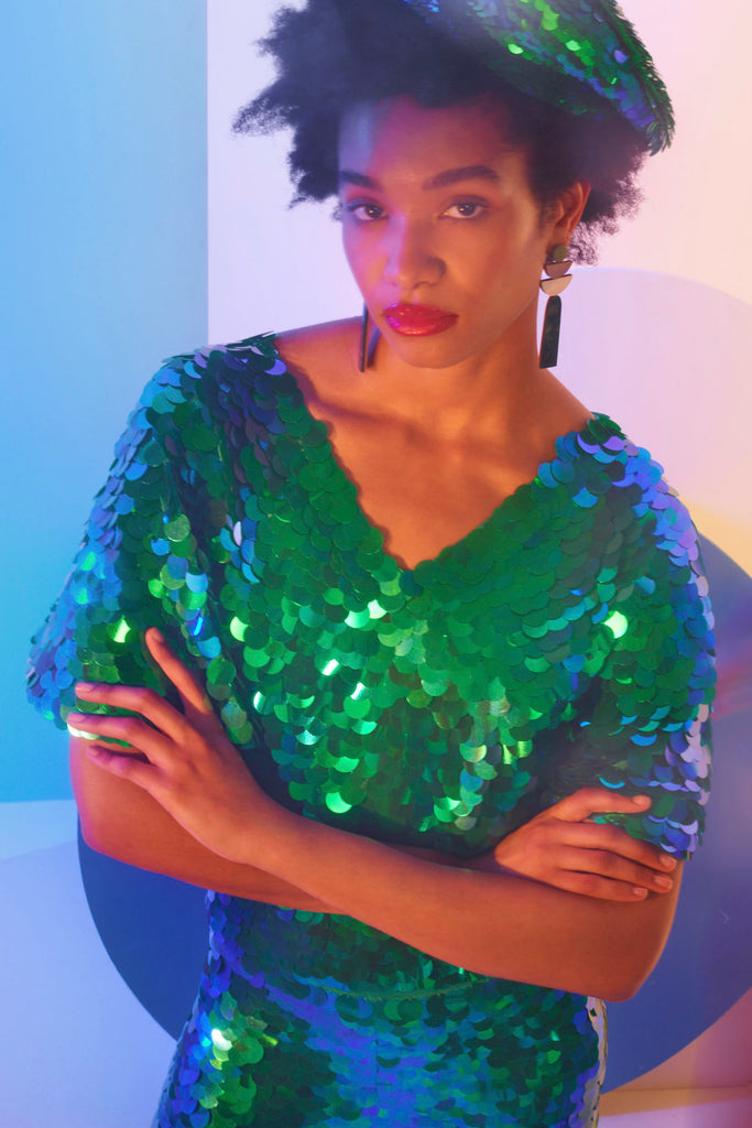 Model with afro hair and red lipstick posing in low light wearing an emerald green Rosa Bloom sequin beret and a Rosa Bloom Emerald green sequin cape top